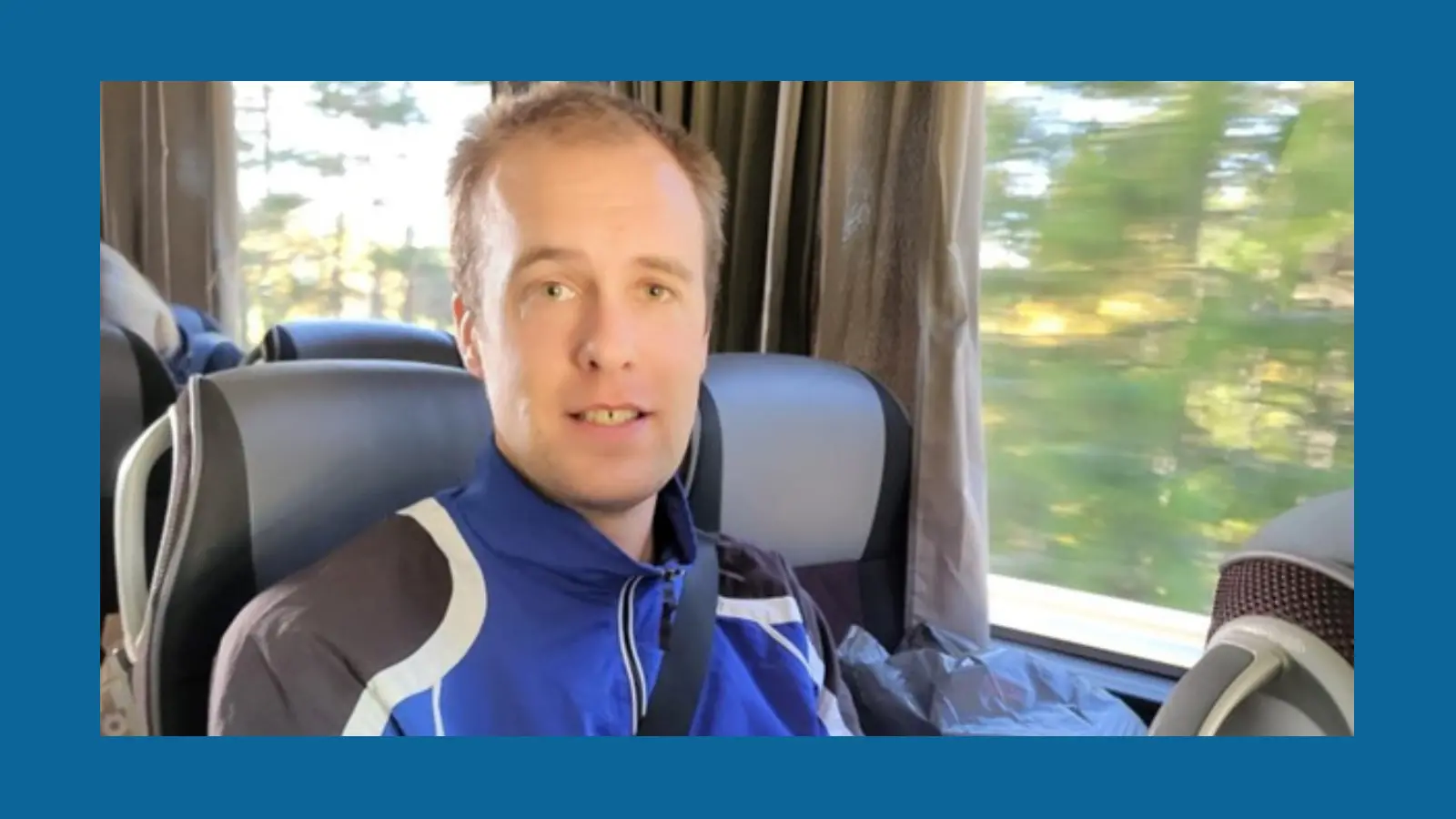 En kille i blå träningsjacka sitter i en buss som åker framåt