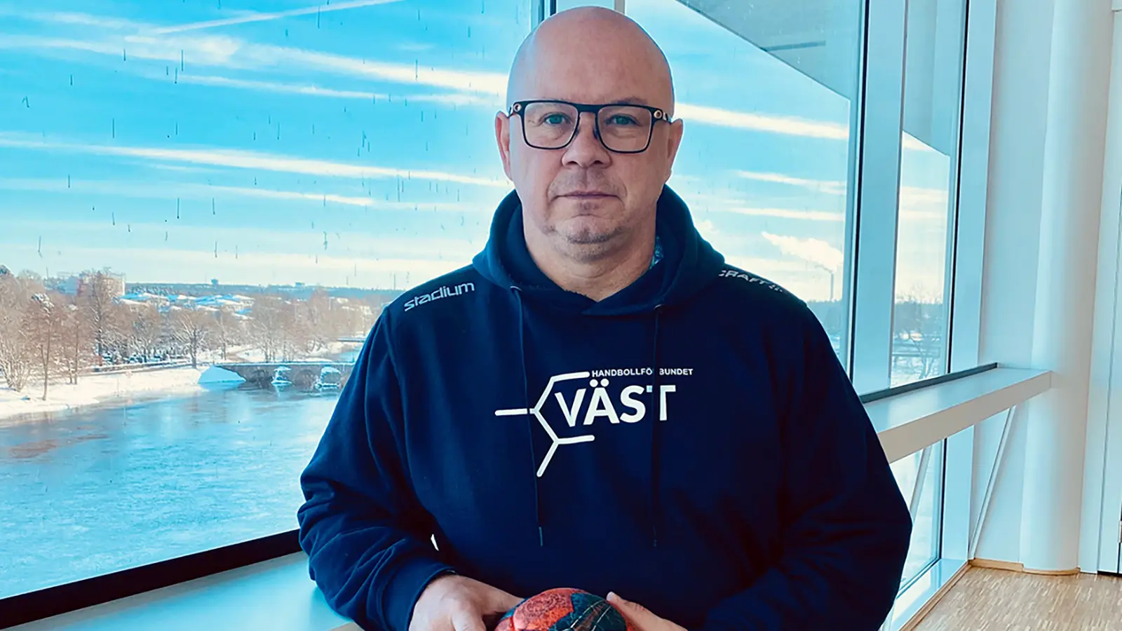 ett foto av en man står och håller i en handboll med båda händerna framför sig och han har på sig en hood-tröja där det står Väst på vilket är Handbollförbundet Västs logga.