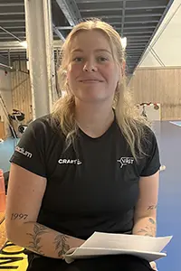en halvkroppsbild på en kvinna som sitter ner med papper i knät som ler lite och tittar rakt fram